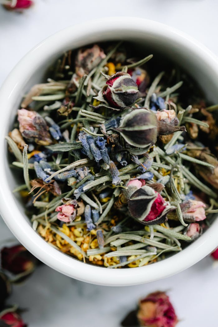 A close-up view of a dried floral and herbal mixture in a white ceramic bowl.